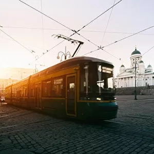 Tram passing Helsinki Senate Square during sunset with Helsinki Cathedral in the background at Finland